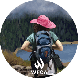 A hiker with a bag of gear and a bright pink hat watches a smoke haze over a forest.